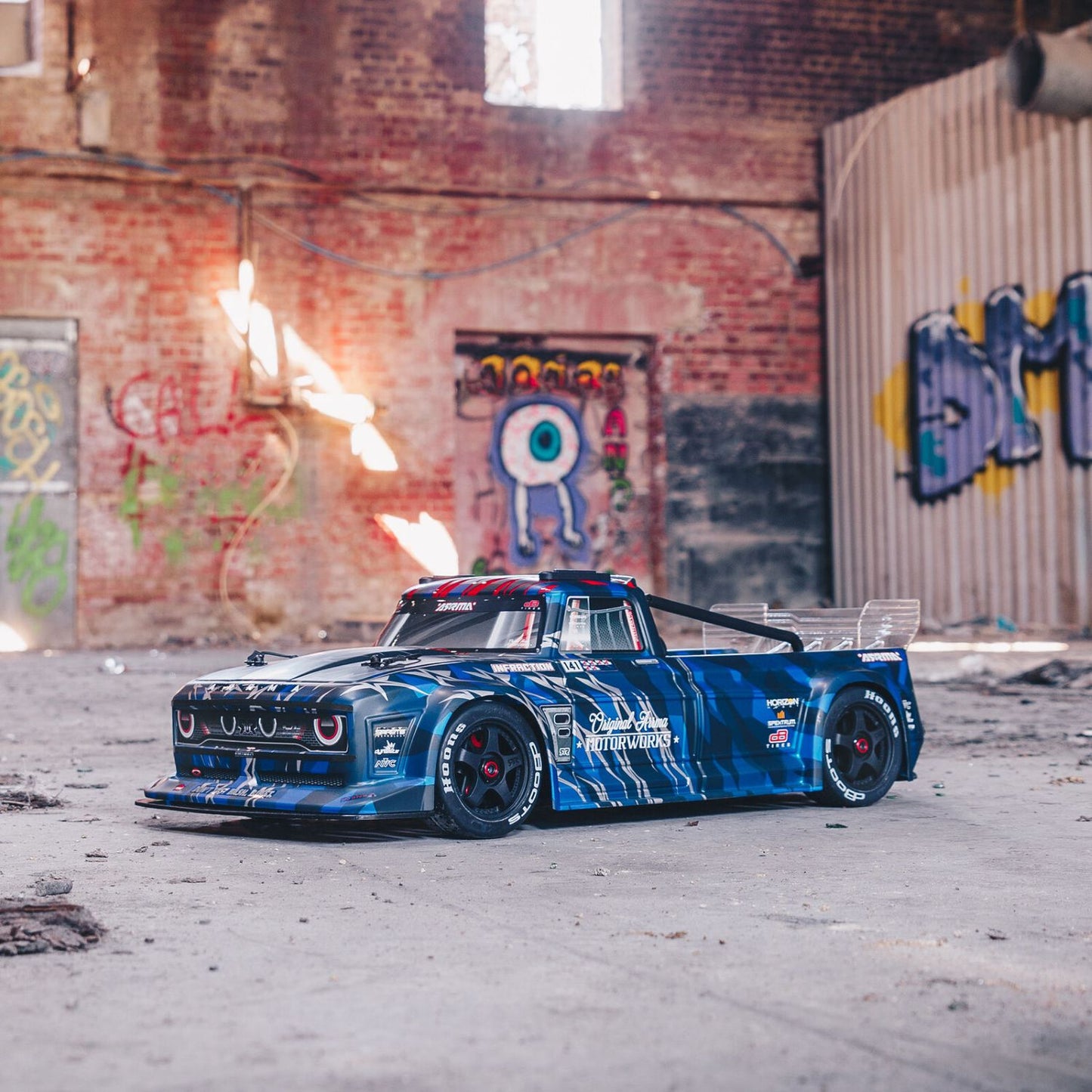1/7 ARRMA INFRACTION 6S AVC 4X4 RTR - Blue race car in an urban setting with graffiti on the wall
