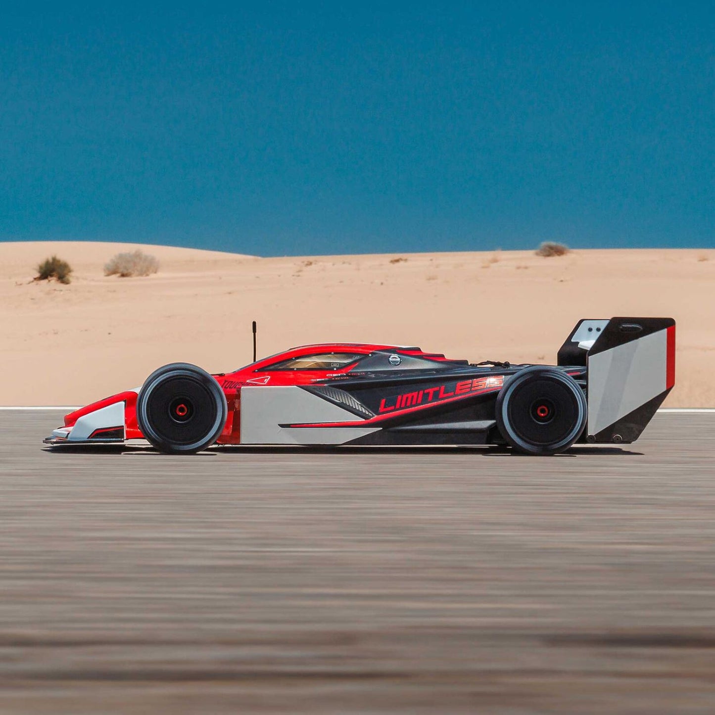 1/7 ARRMA LIMITLESS 120 8S AVC 4X4 RTR - Red and white racing car on a desert track with clear blue sky