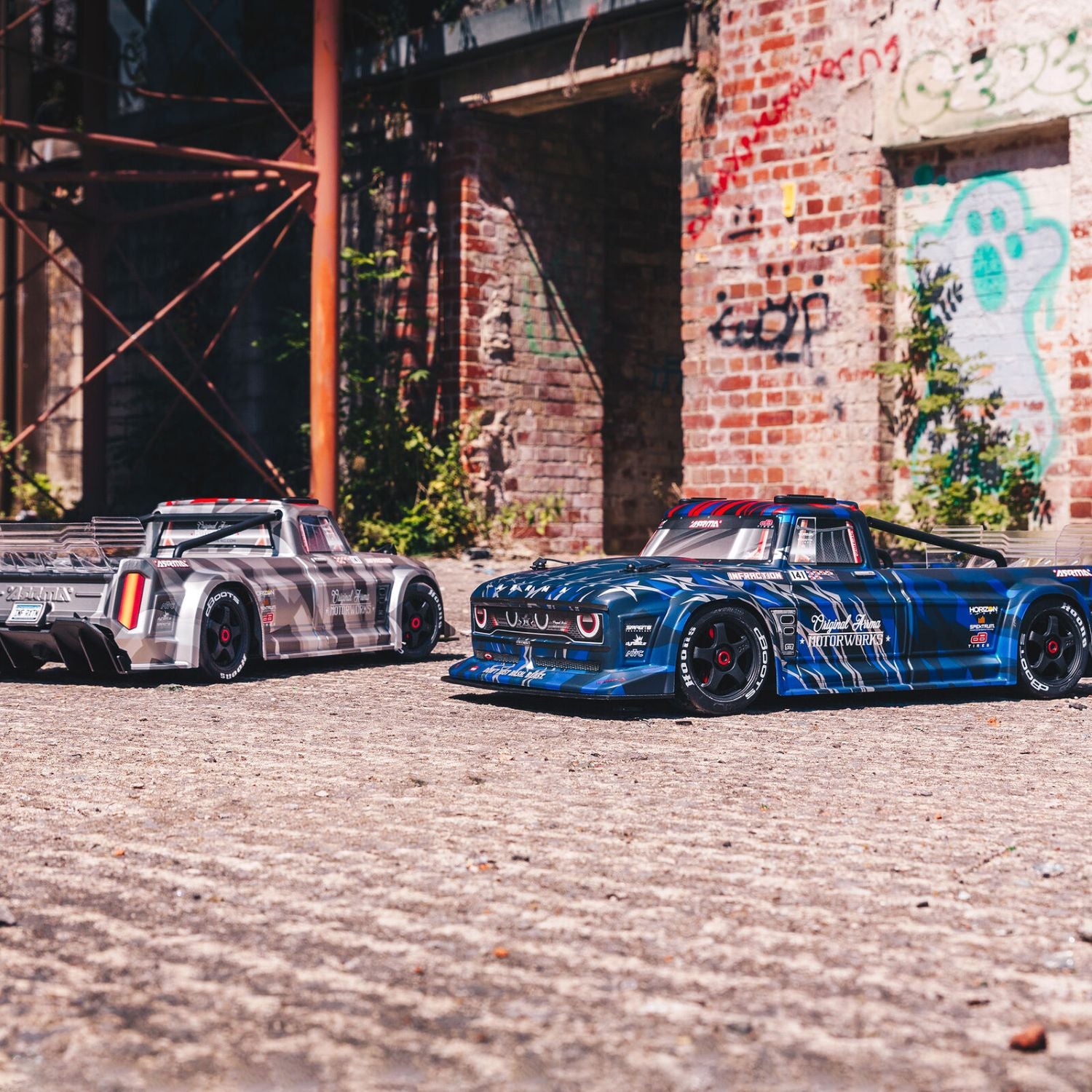 1/7 ARRMA INFRACTION 6S AVC 4X4 RTR - Two modified cars parked in front of a brick wall with graffiti.